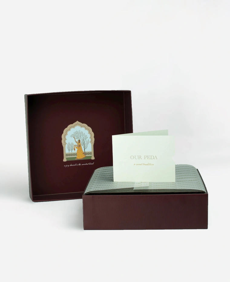 Inside a Ladoomail 9-piece peda gift box: the hand-drawn Ragini Vasanti artwork on the lid, a menu card, a personalised gift card and a butter paper seal.