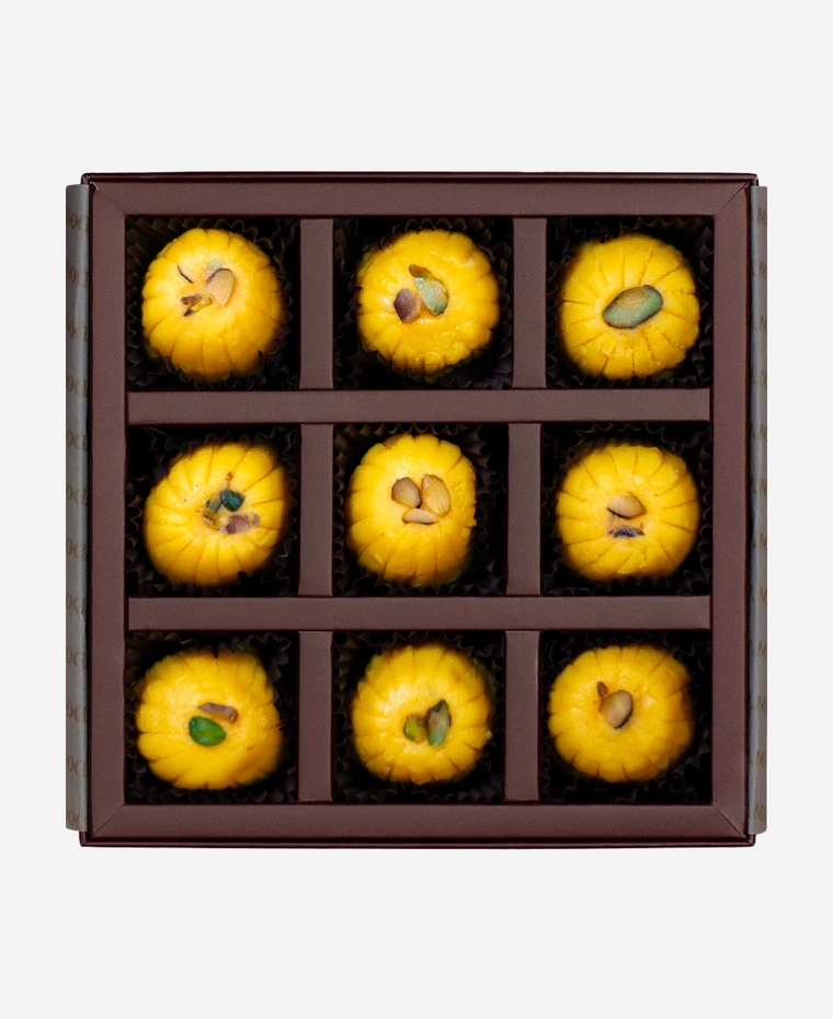 Kesar Peda gift box, 9 pieces, open: saffron-gold kesar peda finished with pistachio in a burgundy box with gold foil lettering.