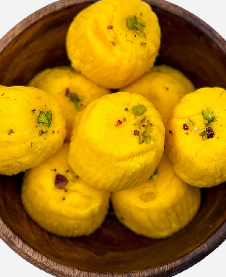 Close-up of handmade saffron-gold kesar peda finished with pistachio, in a wooden bowl.