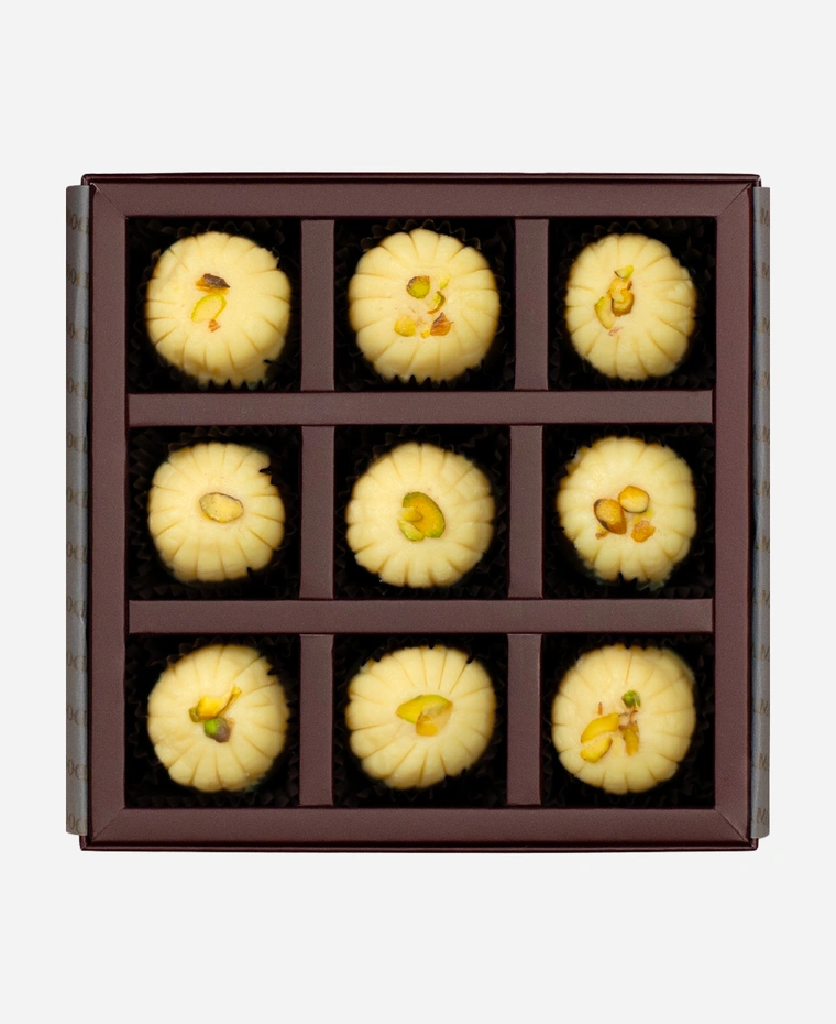 Khoya Peda gift box, 9 pieces, open: ivory khoya peda finished with pistachio in a burgundy box with gold foil lettering.
