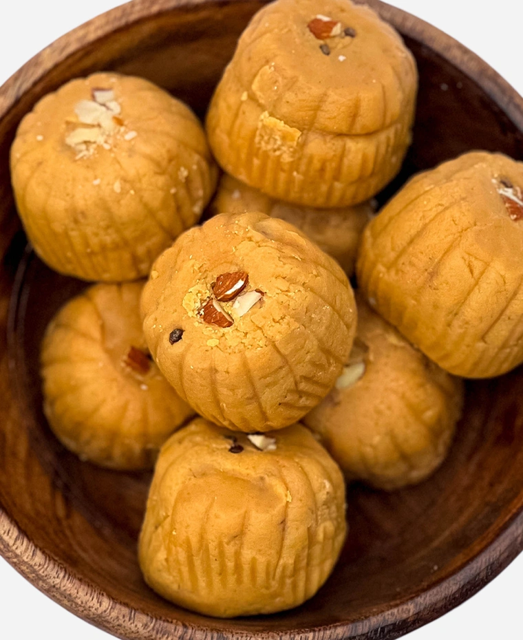 Close-up of handmade caramel-brown ridged Mathura peda finished with almond, in a wooden bowl.