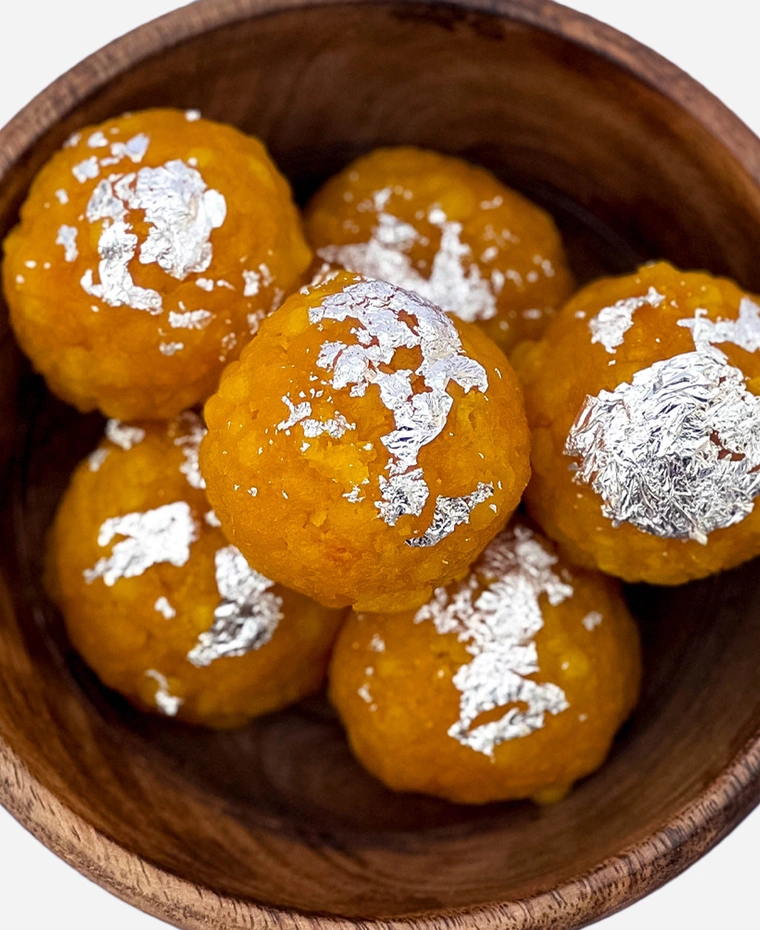 Close-up of handmade golden boondi ladoo topped with edible silver leaf.