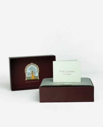 Inside a Ladoomail 6-piece ladoo gift box: the hand-drawn Ragini Vasanti artwork on the lid, a menu card, a personalised gift card and a butter paper seal.