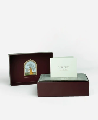 Inside a Ladoomail 6-piece peda gift box: the hand-drawn Ragini Vasanti artwork on the lid, a menu card, a personalised gift card and a butter paper seal.