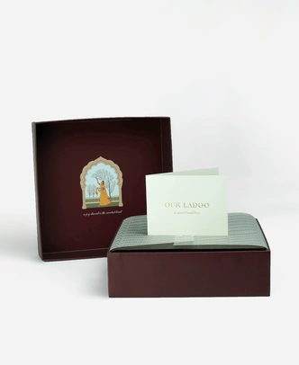 Inside a Ladoomail 9-piece ladoo gift box: the hand-drawn Ragini Vasanti artwork on the lid, a menu card, a personalised gift card and a butter paper seal.