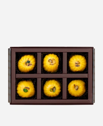 Kesar Peda gift box, 6 pieces, open: saffron-gold kesar peda finished with pistachio in a burgundy box with gold foil lettering.