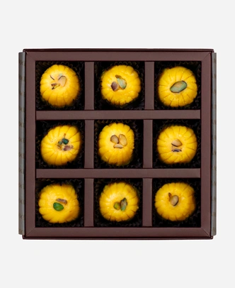 Kesar Peda gift box, 9 pieces, open: saffron-gold kesar peda finished with pistachio in a burgundy box with gold foil lettering.