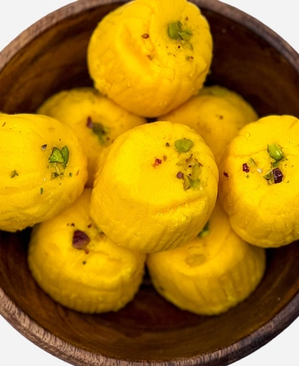 Close-up of handmade saffron-gold kesar peda finished with pistachio, in a wooden bowl.