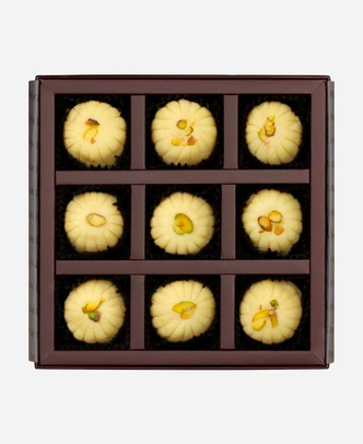 Khoya Peda gift box, 9 pieces, open: ivory khoya peda finished with pistachio in a burgundy box with gold foil lettering.