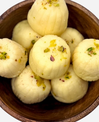 Close-up of handmade ivory khoya peda finished with pistachio and rose petal, in a wooden bowl.