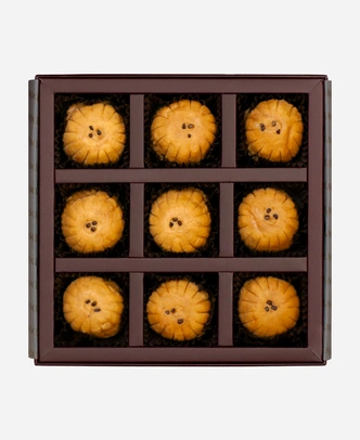 Mathura Peda gift box, 9 pieces, open: caramel-brown Mathura peda in a burgundy box with gold foil lettering.