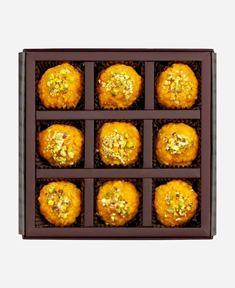 Pistachio Boondi Ladoo gift box, 9 pieces, open: golden boondi ladoo topped with chopped pistachio in a burgundy box with gold foil lettering.