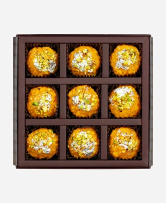 Silver Leaf & Pistachio Boondi Ladoo gift box, 9 pieces, open: golden boondi ladoo topped with edible silver leaf and chopped pistachio in a burgundy box with gold foil lettering.