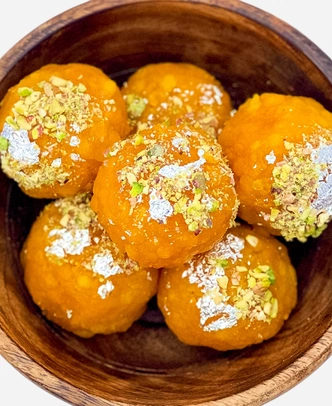Close-up of handmade golden boondi ladoo topped with edible silver leaf and chopped pistachio.