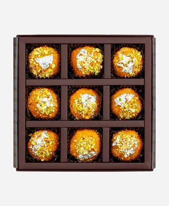 Silver Leaf & Pistachio Motichoor Ladoo gift box, 9 pieces, open: fine-grained motichoor ladoo topped with edible silver leaf and chopped pistachio in a burgundy box with gold foil lettering.
