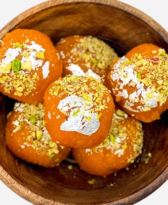 Close-up of handmade fine-grained motichoor ladoo topped with edible silver leaf and chopped pistachio.