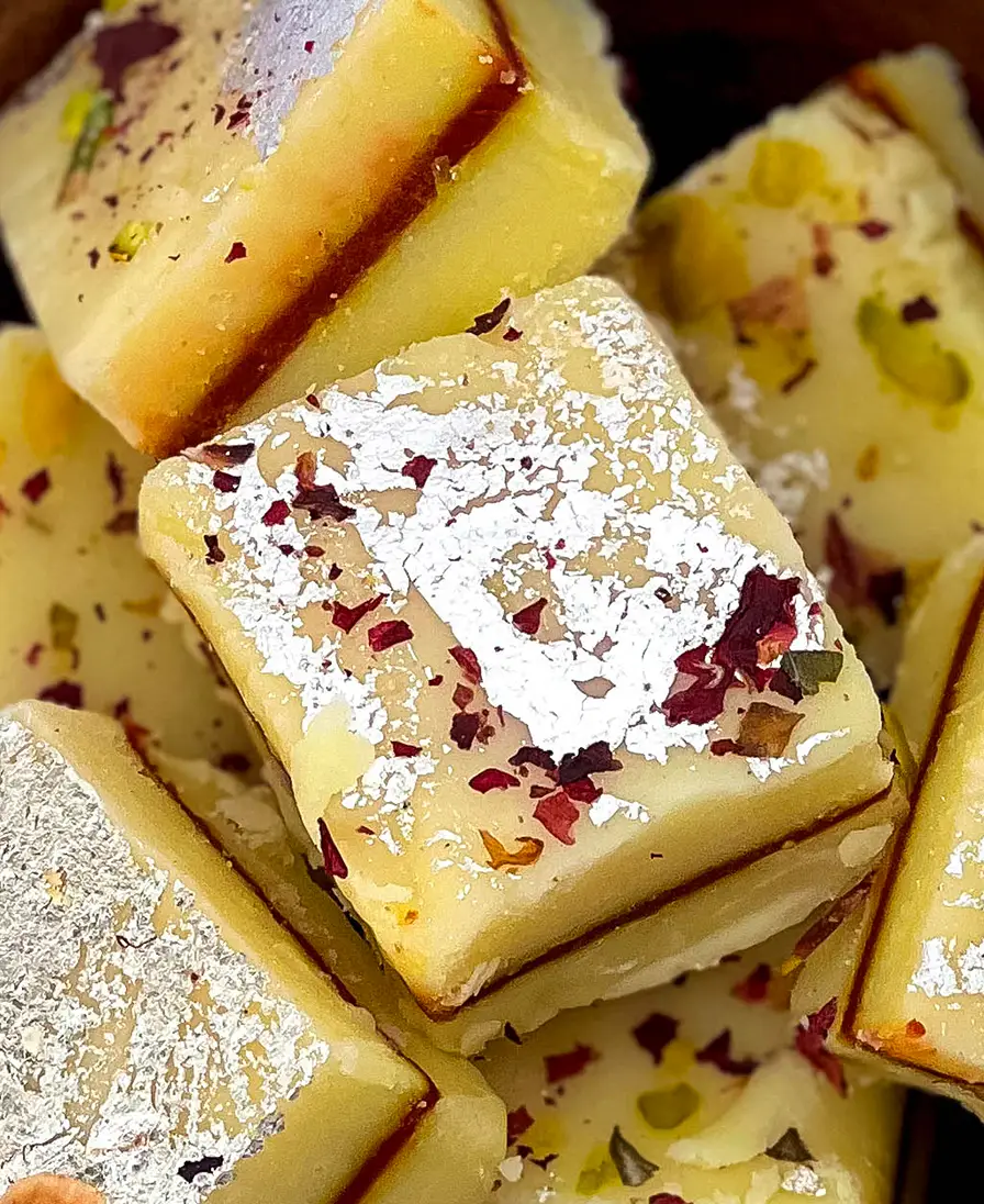 Close-up of silver-leaf topped mithai with rose petals and pistachio.