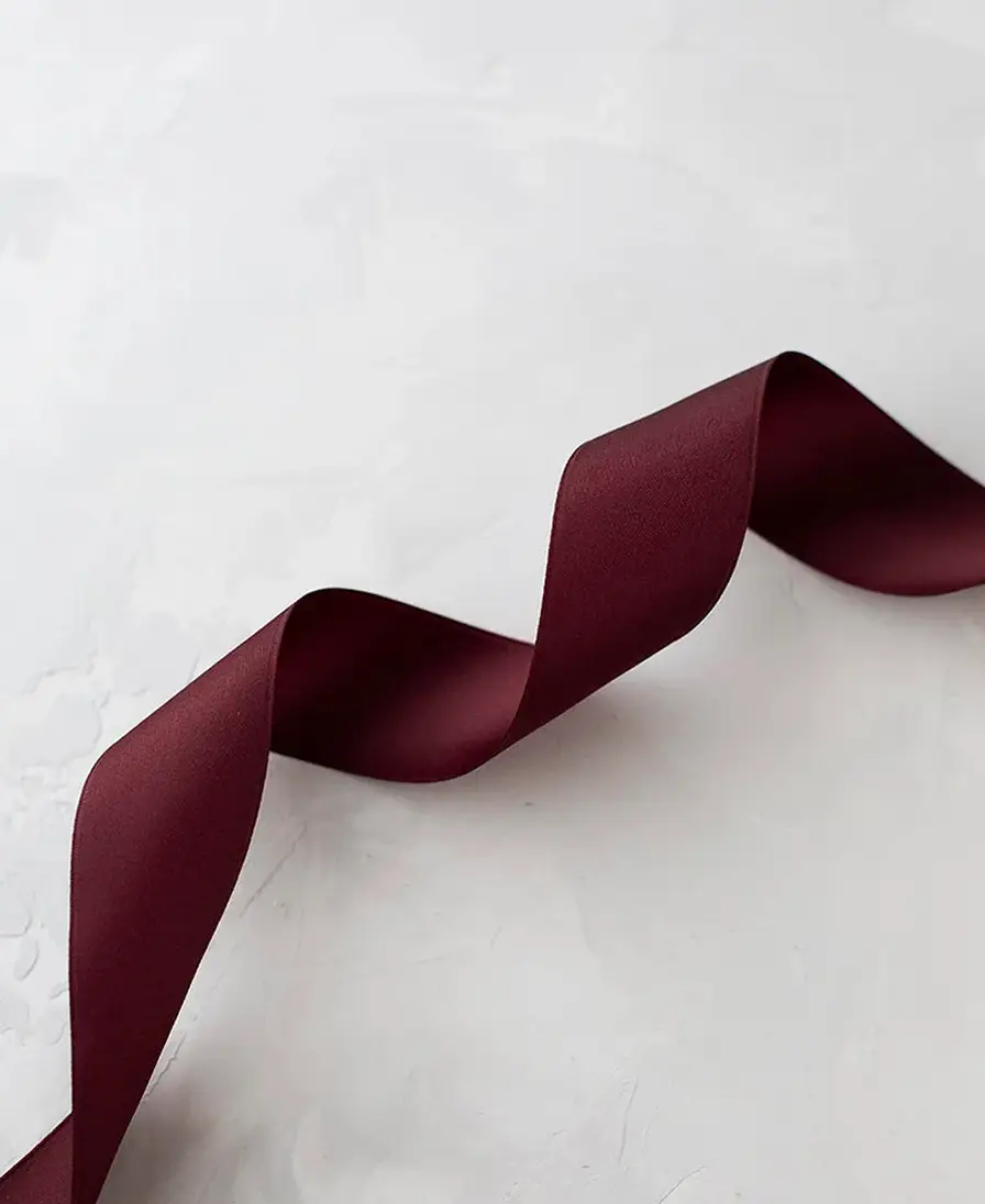 Curled burgundy satin ribbon on a textured grey surface.