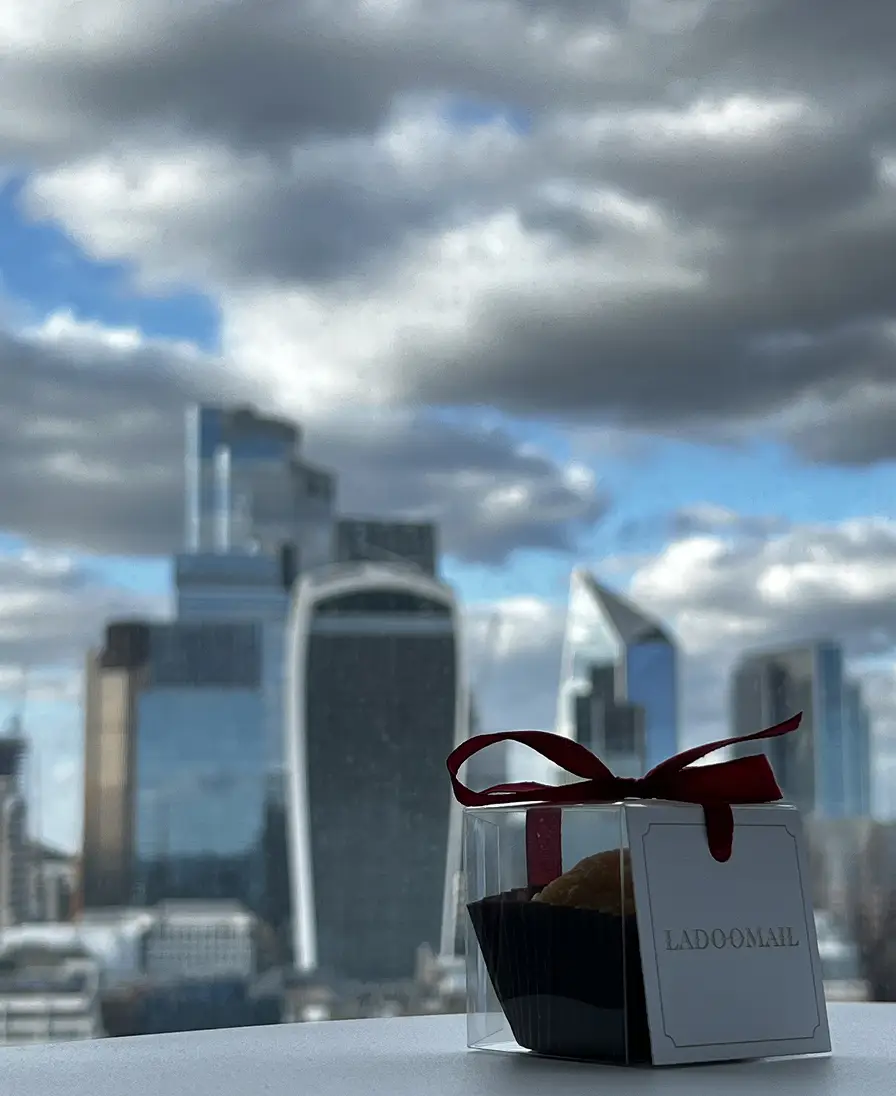 Ladoomail burgundy gift box with red ribbon against the City of London skyline.