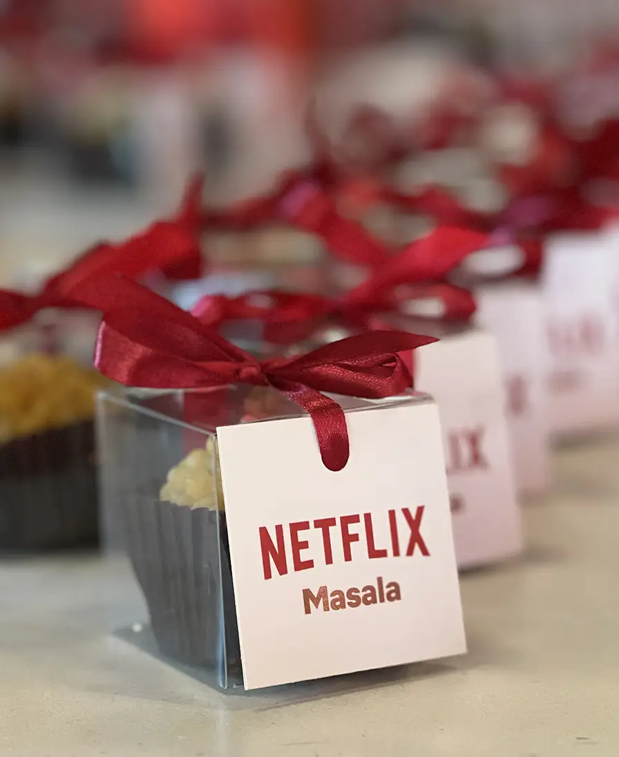 Ladoomail celebration favours branded for Netflix's Masala network, with red ribbon bows among red floral decor.