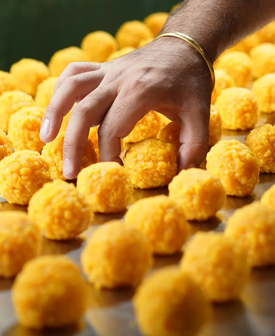 Hand reaching for freshly rolled golden boondi ladoo arranged in rows on a tray.