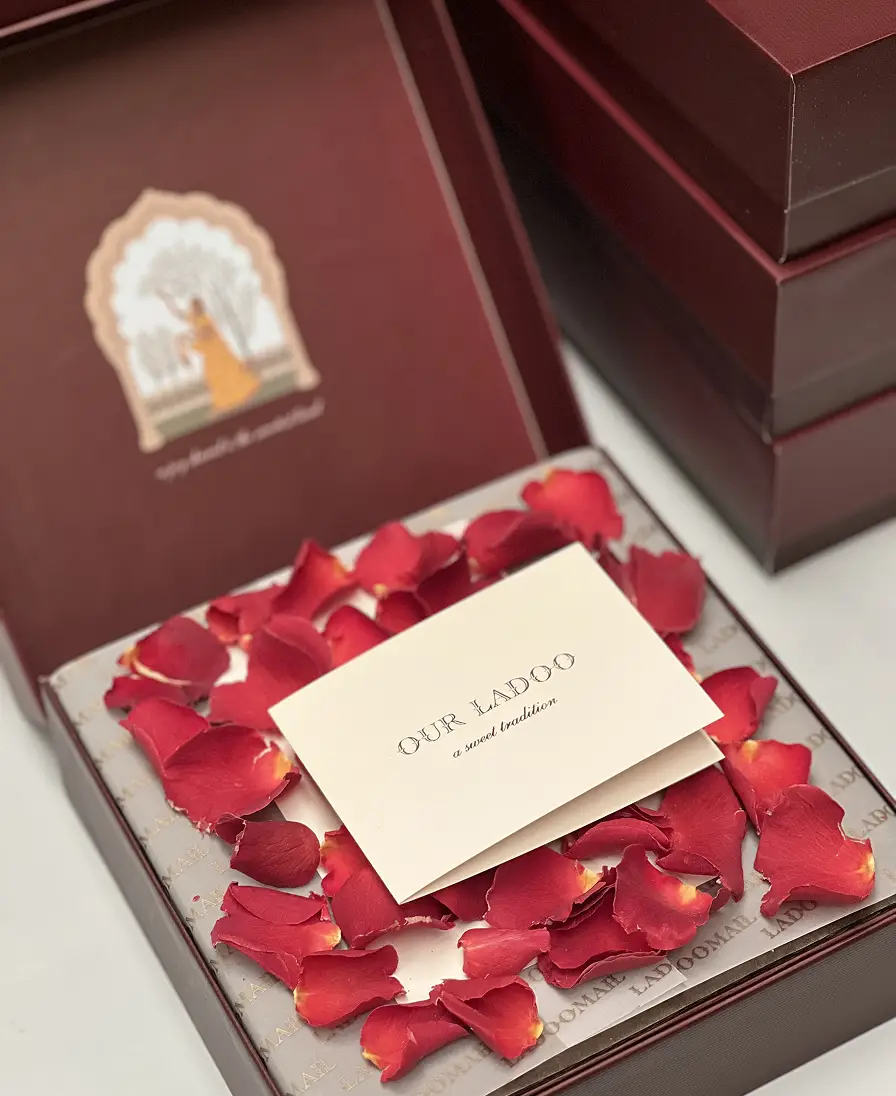 Ladoomail burgundy gift box with gold foil crest, rose petals and an 'Our Ladoo' personalised card.