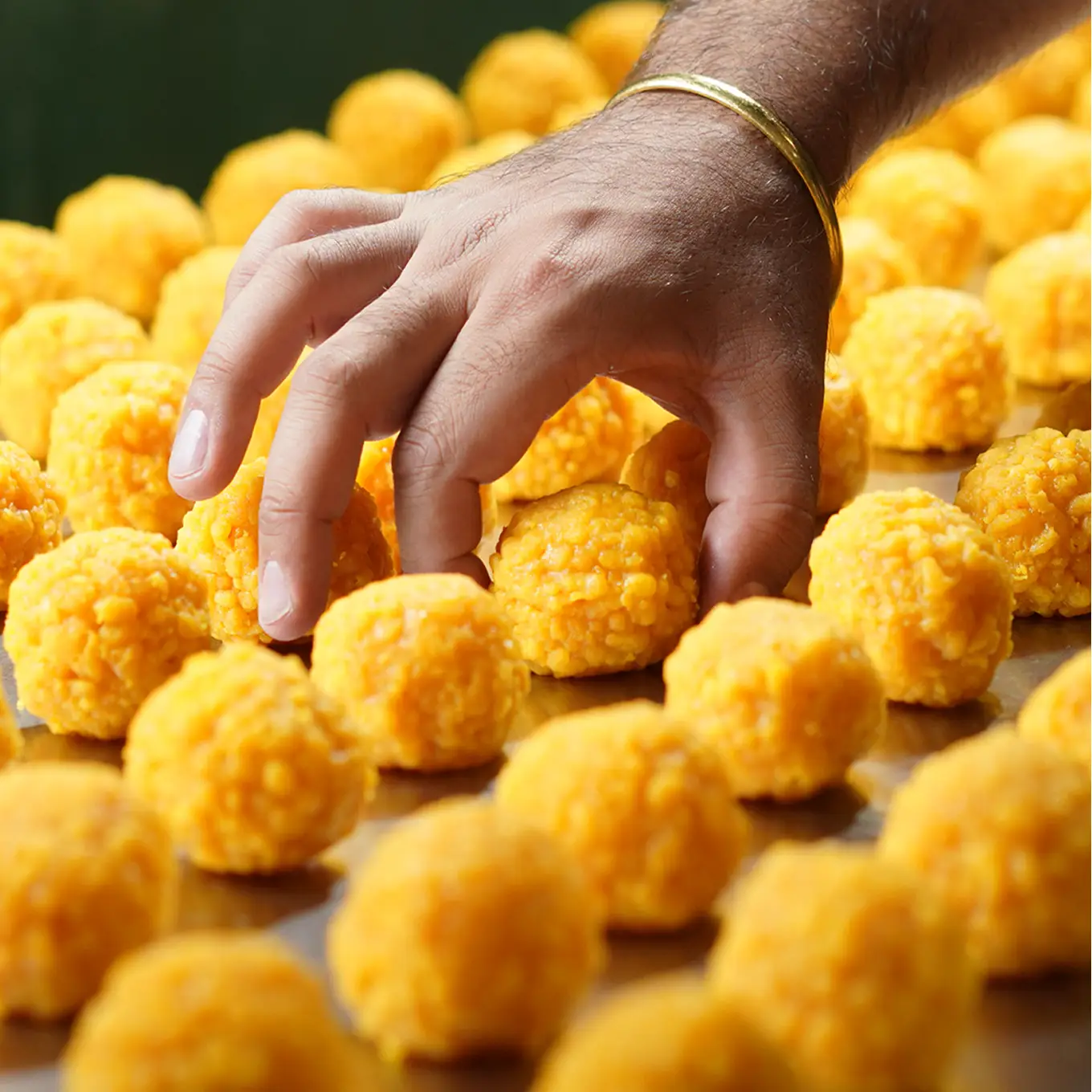 Hand reaching for freshly rolled golden boondi ladoo arranged in rows on a tray.