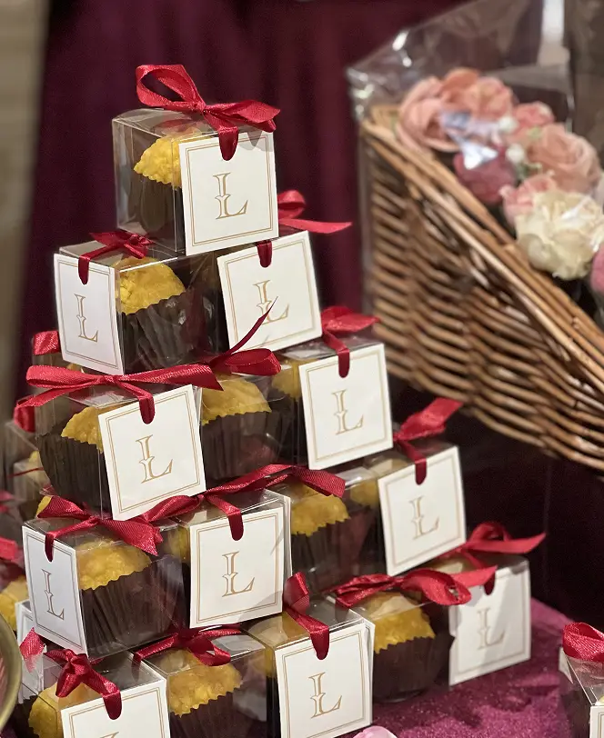 Ladoomail mithai favour boxes tied with red ribbon and personalised gold monogram tags, tiered for a wedding reception.