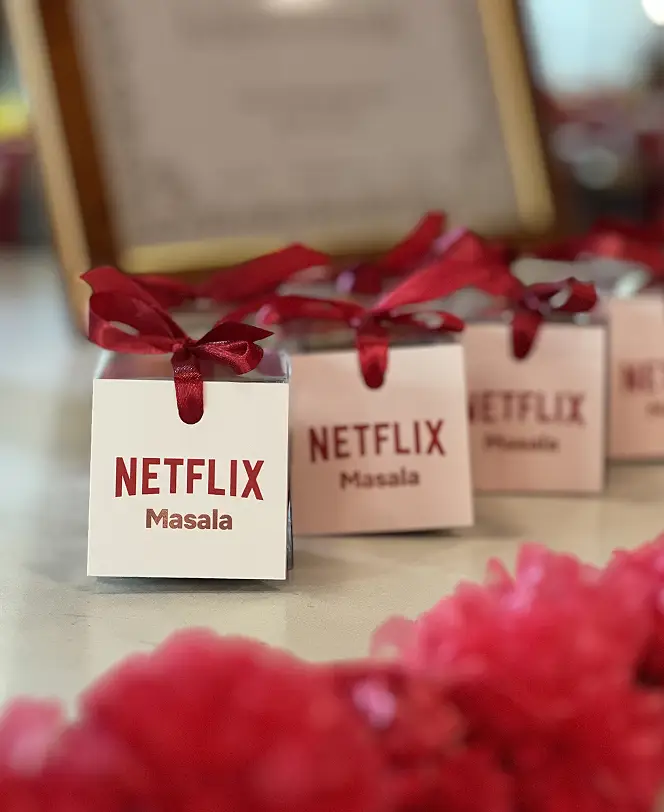 Ladoomail celebration favours branded for Netflix's Masala network, with red ribbon bows among red floral decor.