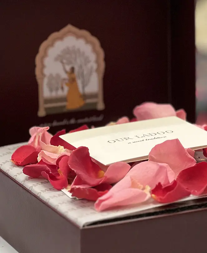Ladoomail burgundy gift box open on rose petals, with a personalised card and the hand-drawn Ragini Vasanti artwork inside the lid.