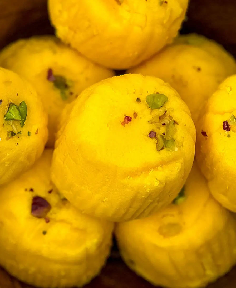 Close-up of handmade saffron-gold kesar peda finished with pistachio, in a wooden bowl.