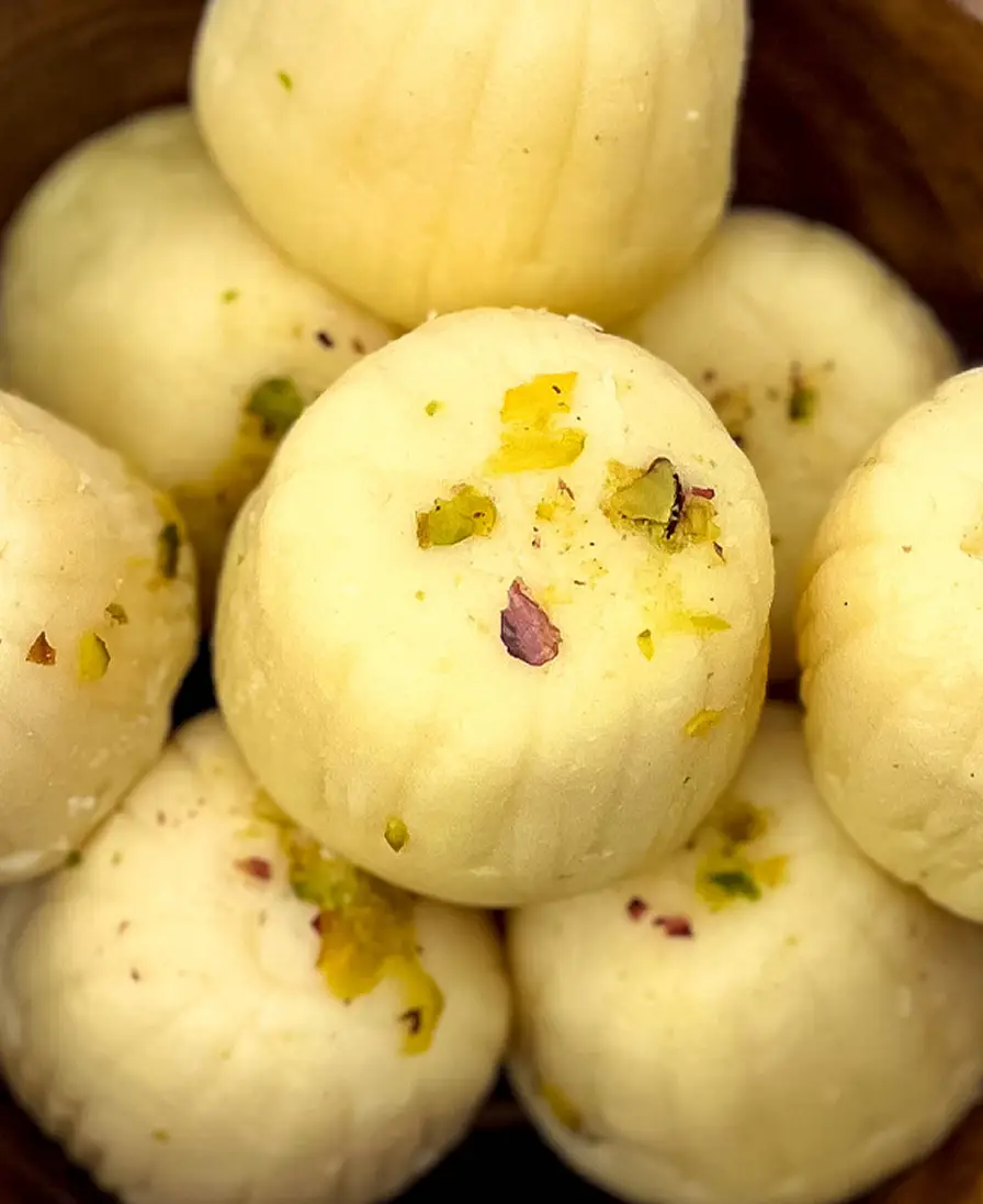 Khoya peda Close-up of handmade ivory khoya peda finished with pistachio and rose petal, in a wooden bowl.