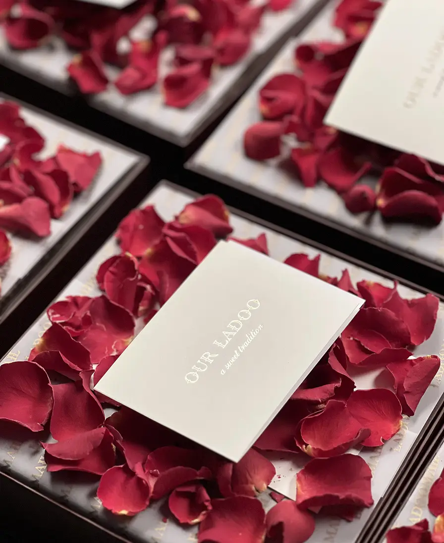 Ladoomail burgundy gift boxes open with rose petals and 'Our Ladoo, a sweet tradition' cards.