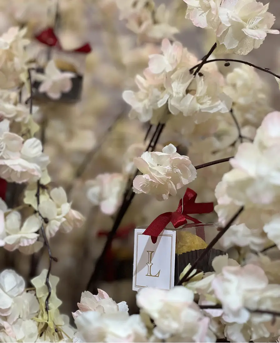 Ladoomail favour tree in white blossom, with a monogrammed favour box among the flowers.
