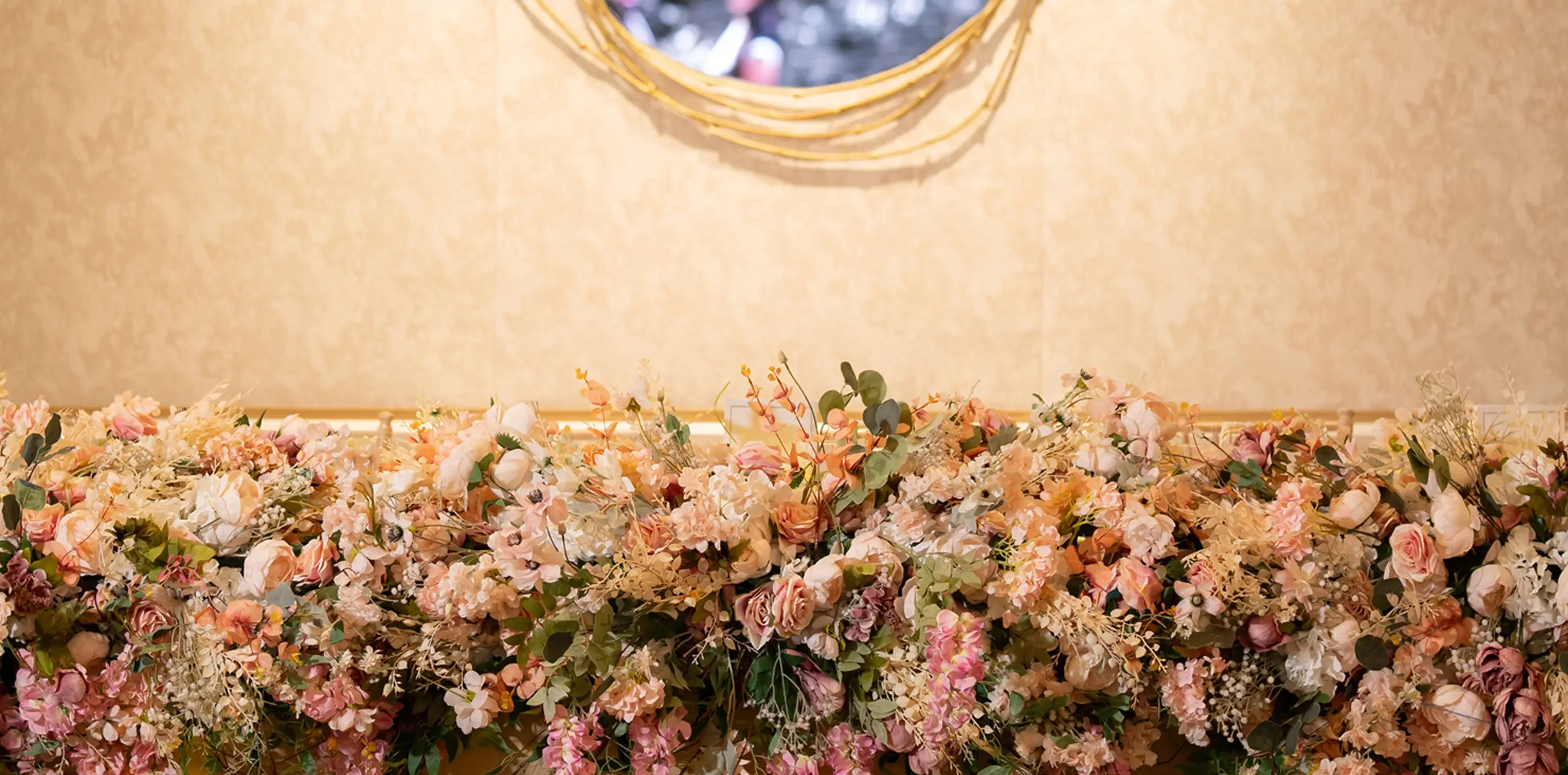 Pastel floral table runner beneath a gold-framed round mirror at a wedding reception.