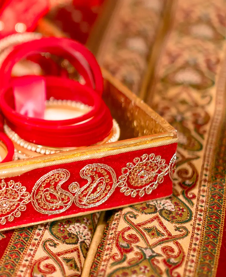 Red and gold bridal bangles in an embroidered tray on traditional sari brocade.