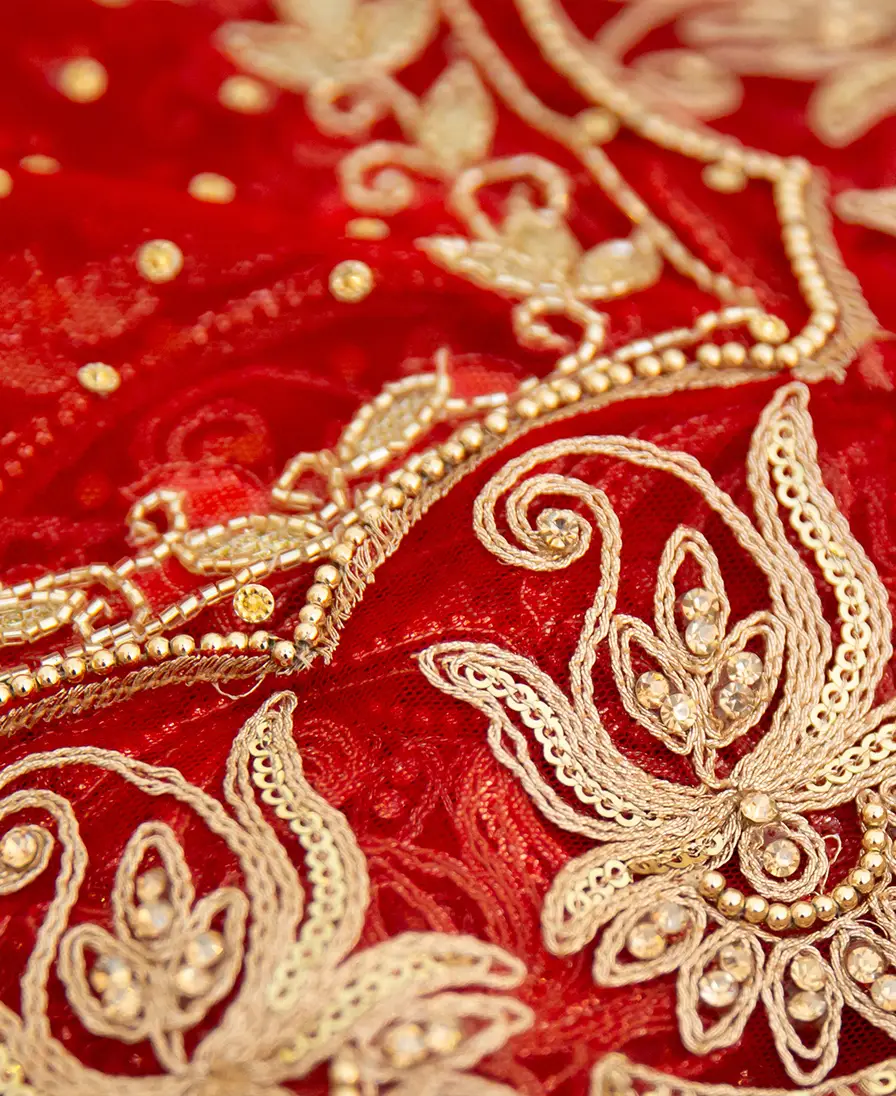 Macro detail of gold embroidery on red bridal fabric.