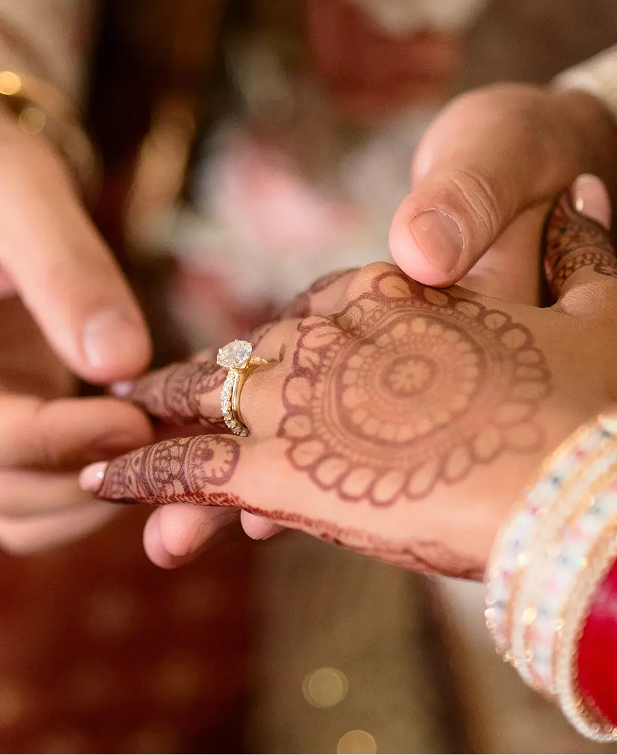 Engagement ring being placed on a henna-decorated hand with bangles.