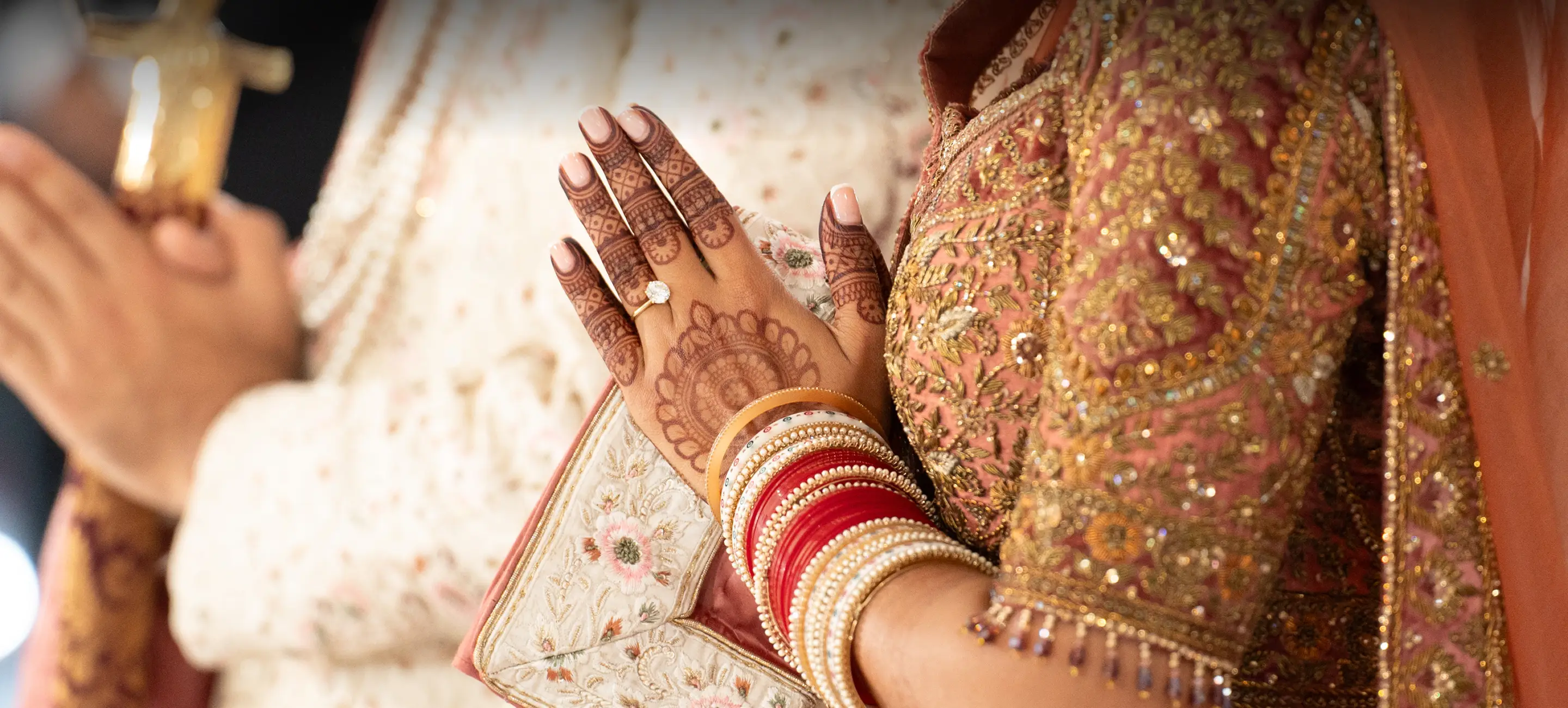 Bride and groom's hands pressed together in blessing, with henna and bridal jewellery.